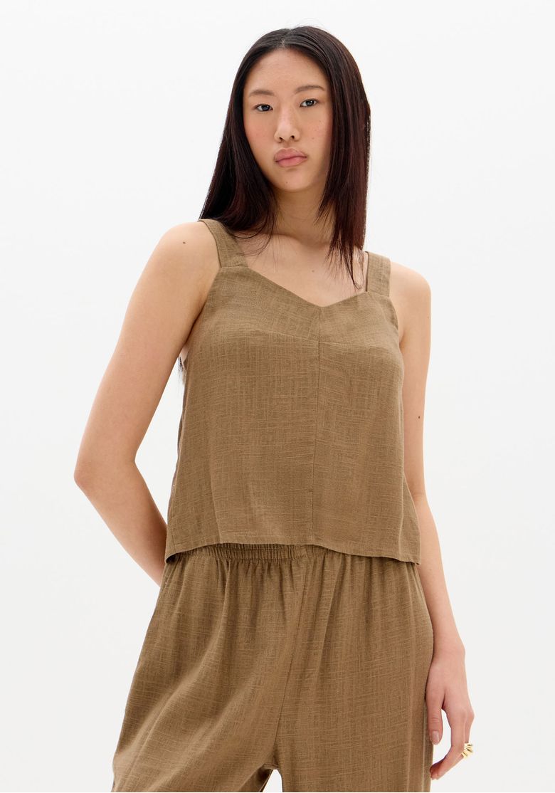 Modelo em 3/4 usando blusa cropped marrom de linho com alças largas, look casual elegante com calça ampla