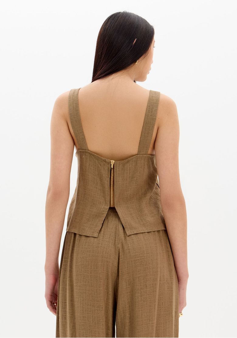 Costas da blusa com zíper aparente dourado e recortes na barra traseira, detalhe do fechamento