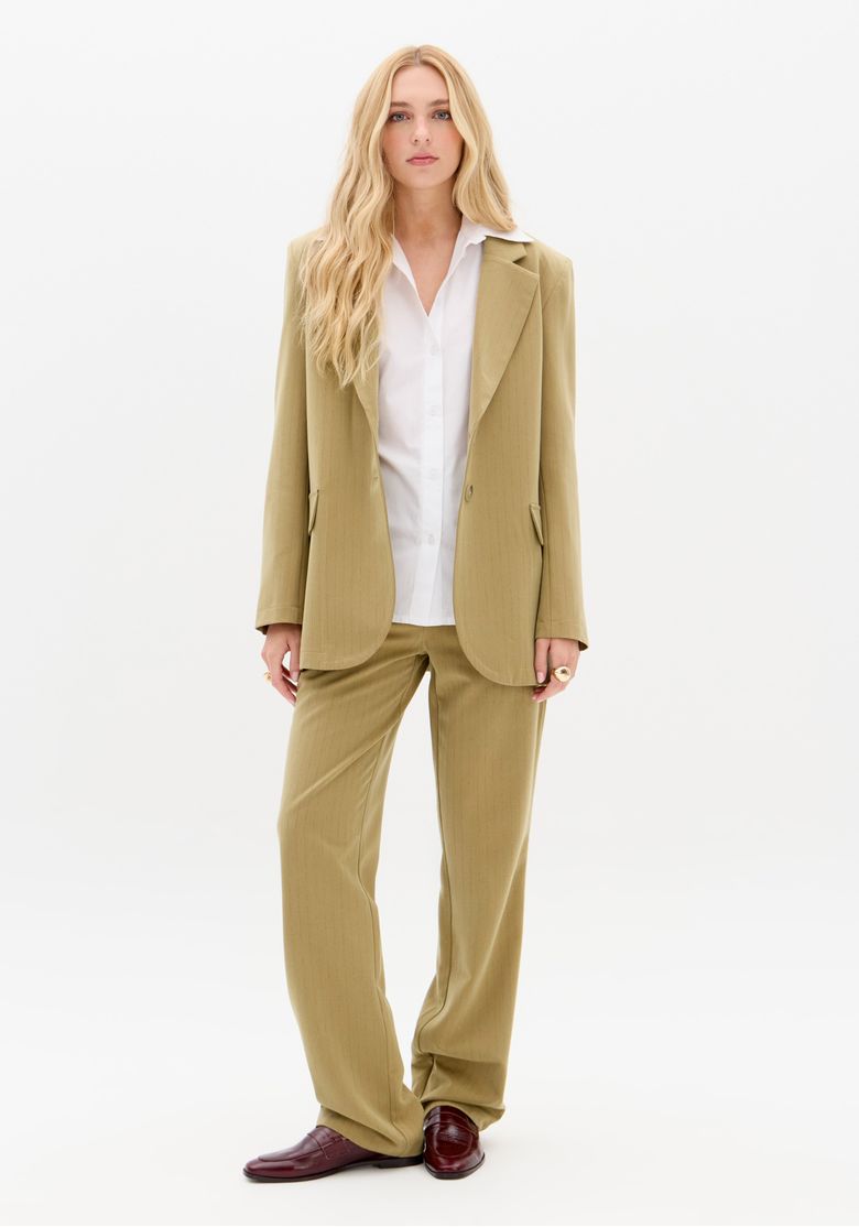Detalhe frontal do blazer oversized em risca de giz verde, mostrando lapela clássica, botões e bolso com aba