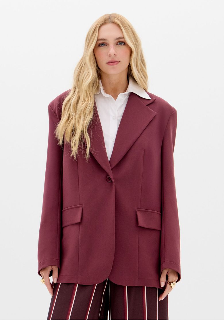 Look urbano ao ar livre com blazer oversize vermelho e calça combinando, styling com cachecol cinza e postura descontraída