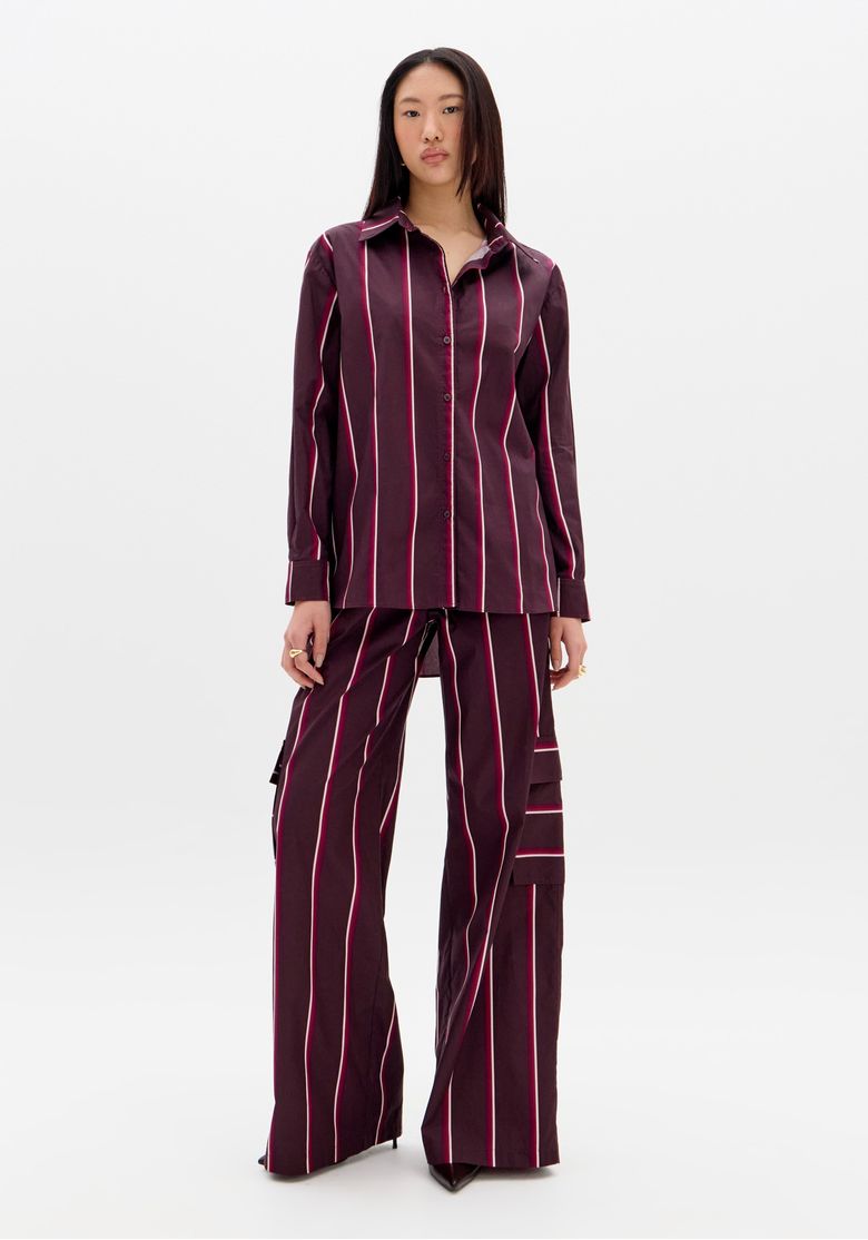 Modelo-em-fundo-branco-vestindo-camisa-feminina-oversized-listrada-vinho-vista-frontal-mostrando-modelagem-ampla-e-mangas-longas