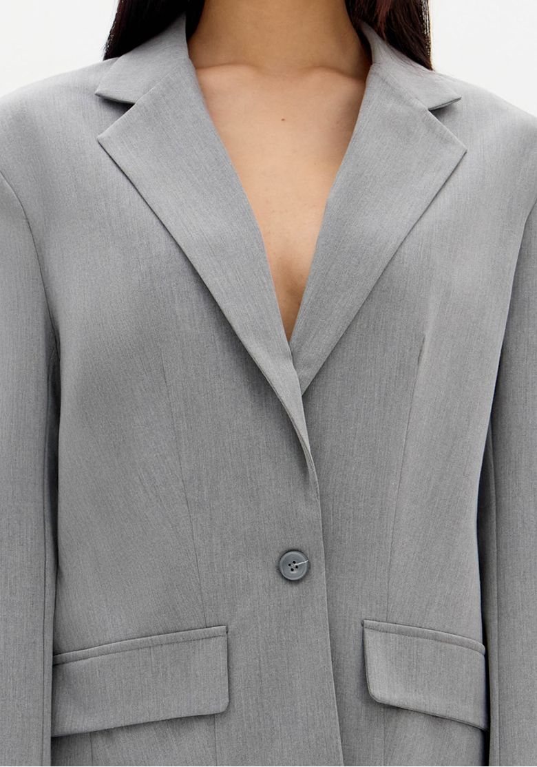 Detalhe da lapela clássica e fechamento por botão do blazer cinza.