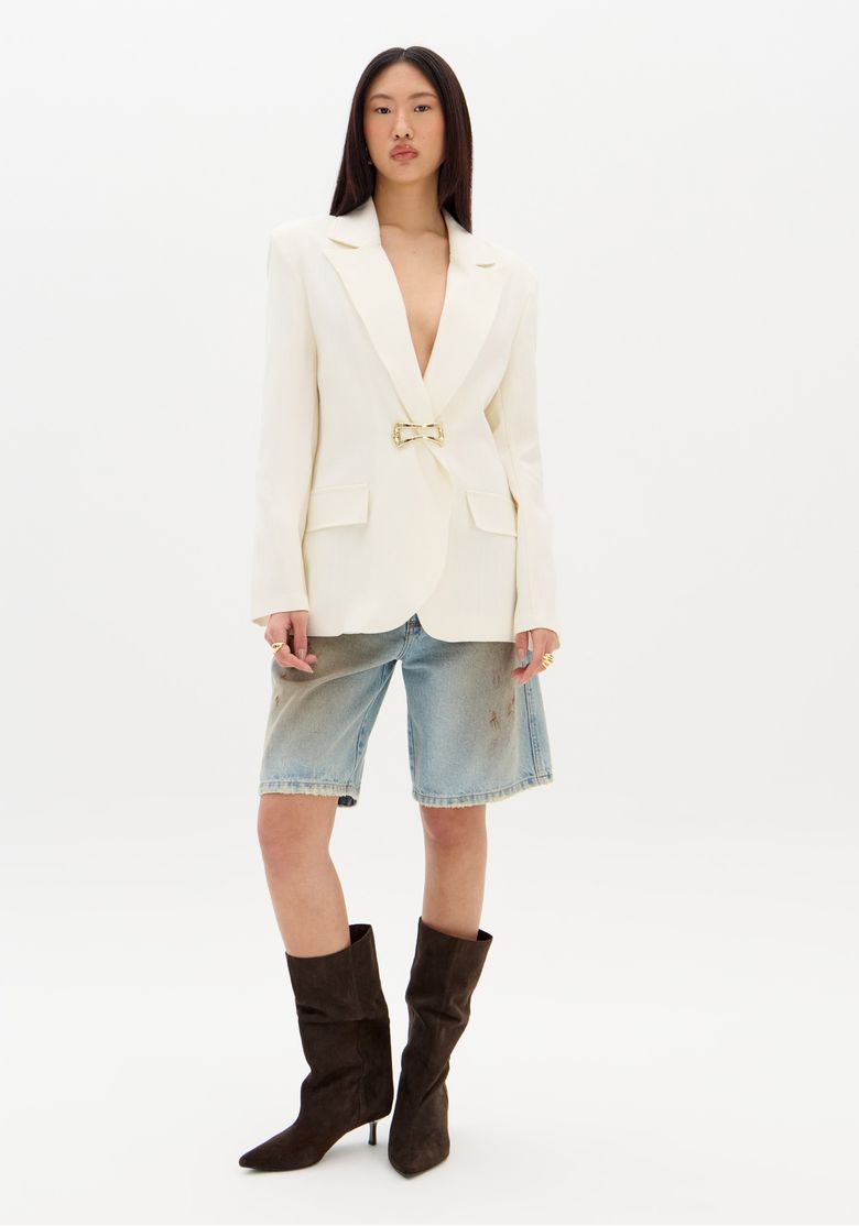 Vista completa do blazer branco com modelagem alongada, combinado com bermuda jeans.