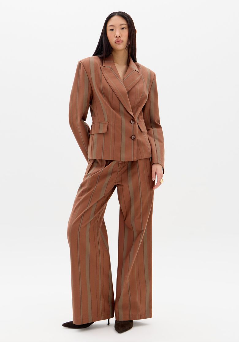Modelo frontal meia altura usando blazer oversized listrado marrom com lapela clássica, bolsos com aba e dois botões frontais
