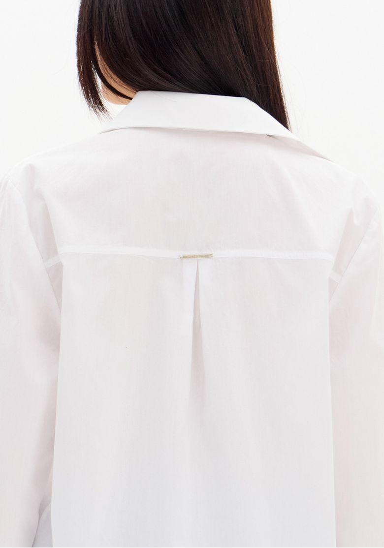Close do detalhe traseiro da camisa branca: pala com prega central e acabamento do tecido tricoline 100% algodão