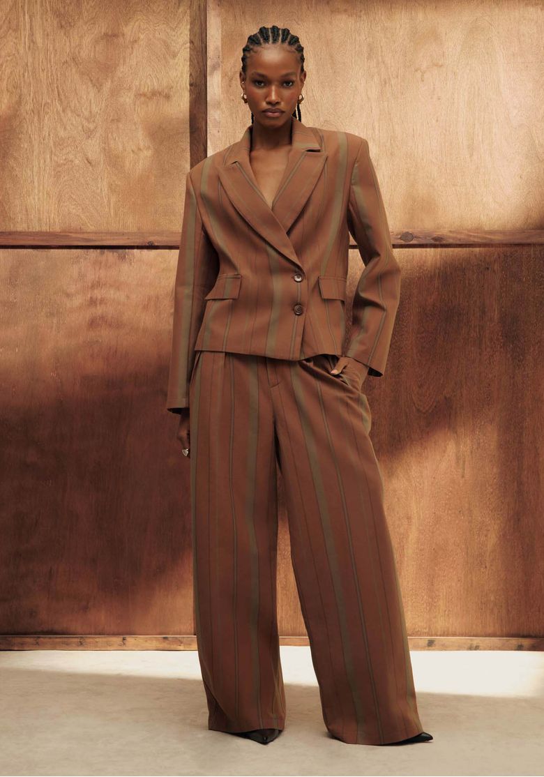 Modelo usando conjunto alfaiataria marrom listrado: blazer e calça reta cintura média em ambiente com painel de madeira