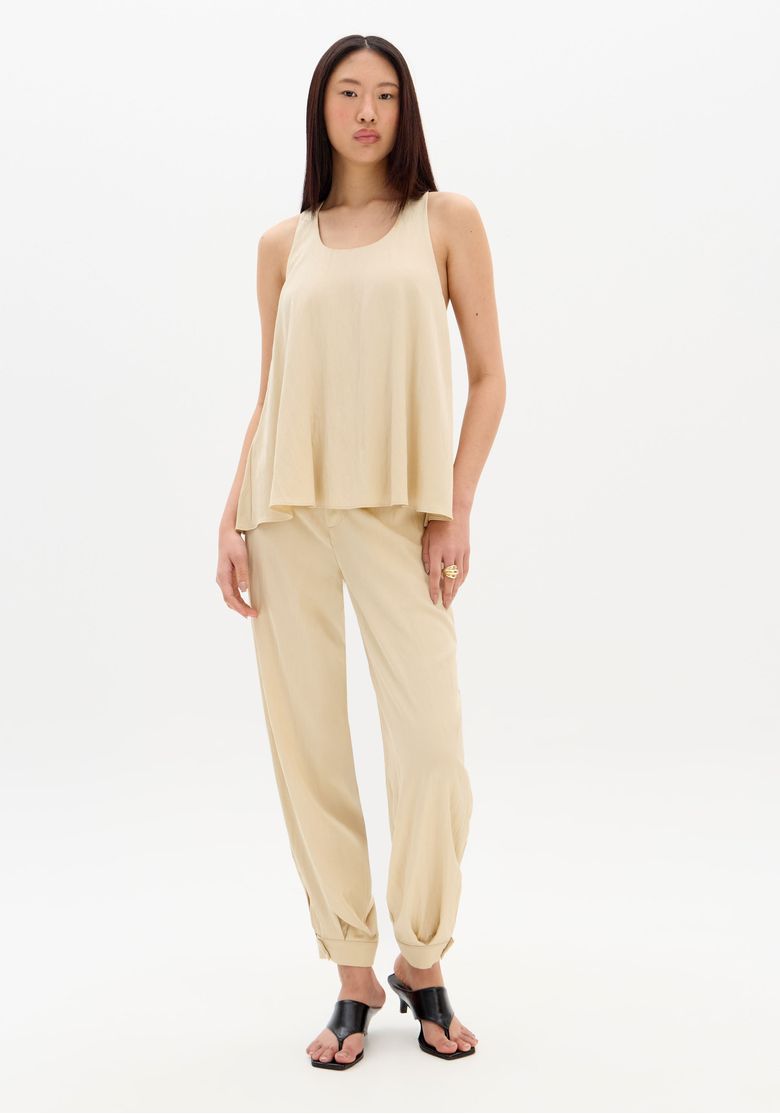Modelo vestindo calça slouchy cintura alta bege com regata solta, look frontal full body mostrando caimento e barra afunilada