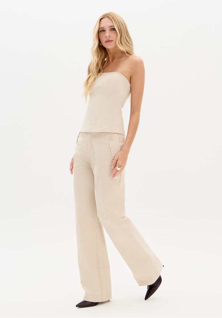 Modelo em estúdio usando calça full length bege cintura média e top tomara-que-caia, vista 3/4 mostrando caimento reto e presença minimalista