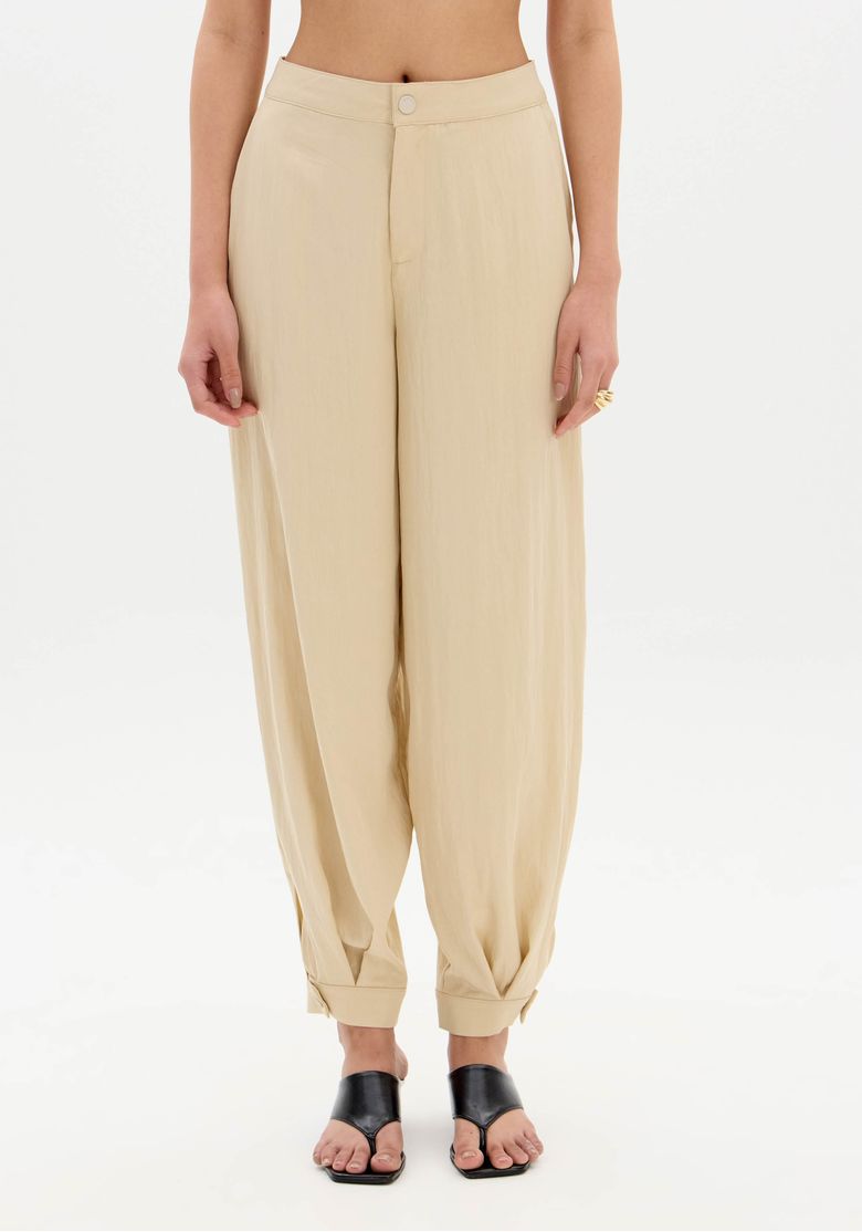Close do tecido plano pesado e da costura traseira da calça slouchy bege, realçando o caimento