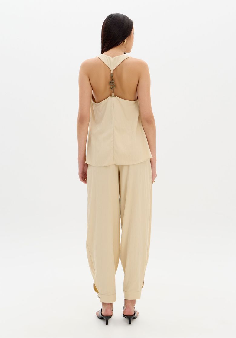 Close do cós frontal e fechamento da calça slouchy bege evidenciando zíper e botão no cós