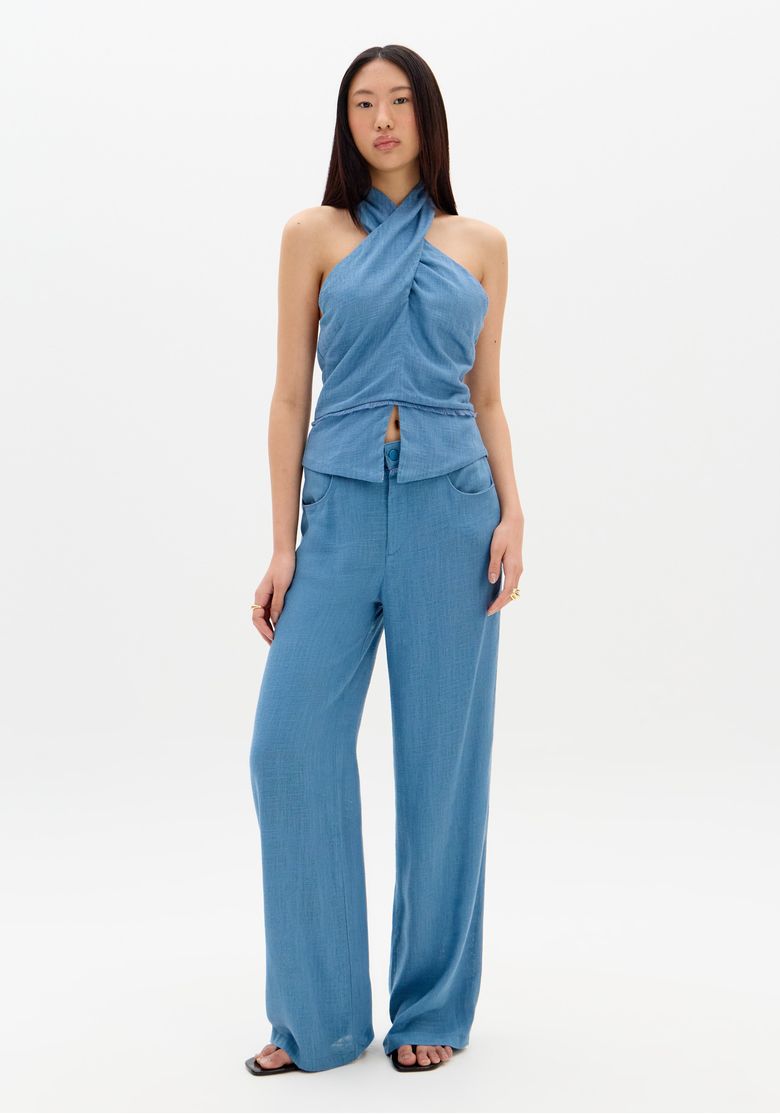 Close frontal da cintura da calça wide leg azul exibindo botão encapado, zíper e bolso faca frontal