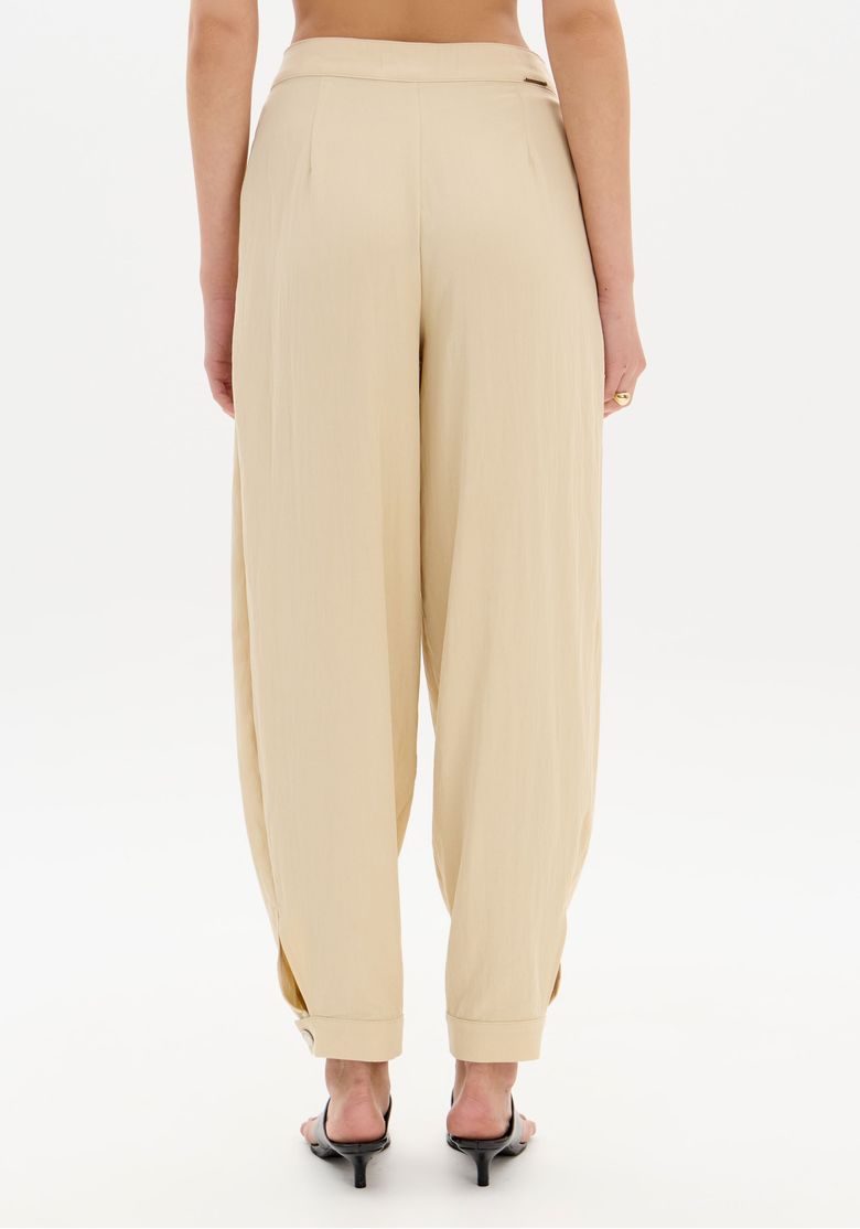 Visão traseira da calça slouchy bege com caimento fluido e barra afunilada vista por trás