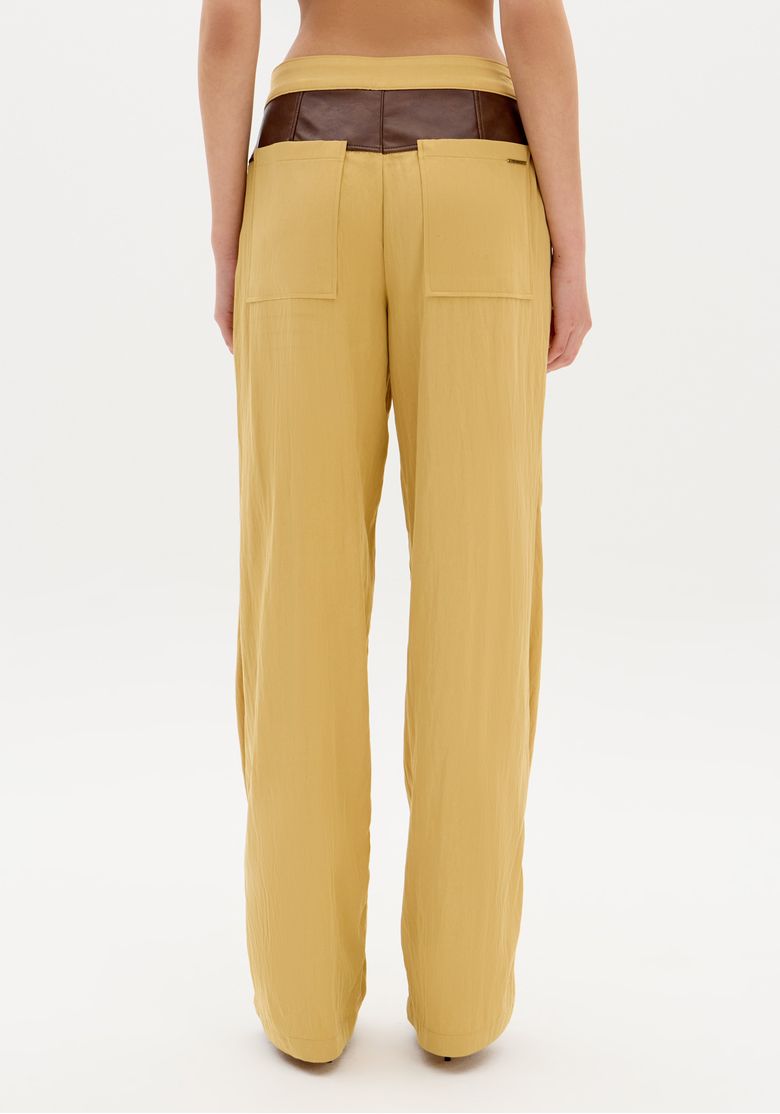 Modelo de costas vestindo a calça wide leg bicolor em ambiente interno.