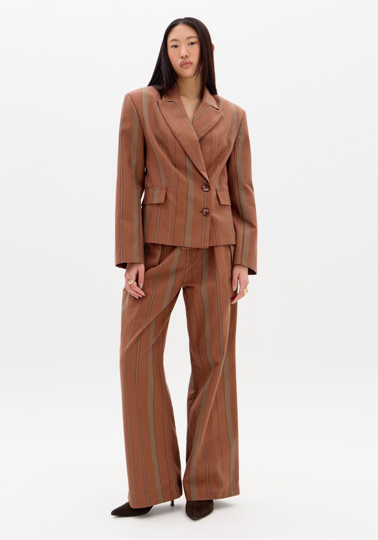 Modelo em pé vestindo blazer e calça reta listrada marrom, look completo com perna ampla e caimento estruturado