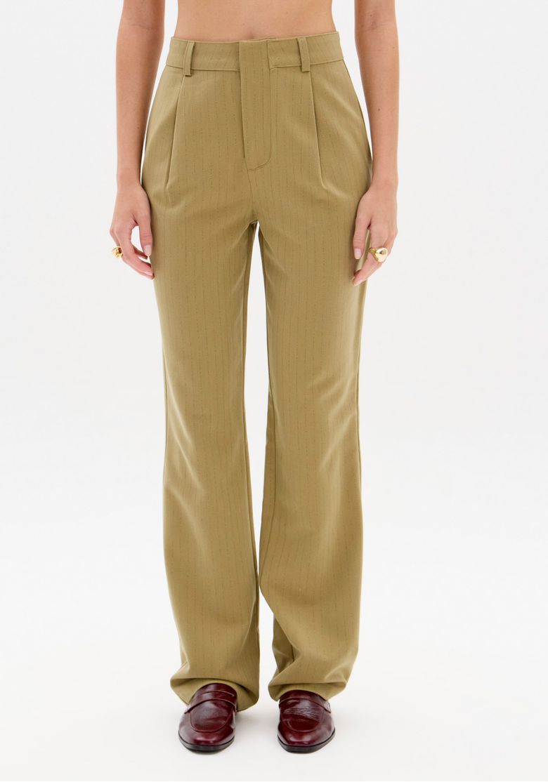 Close frontal da calça full length verde risca de giz mostrando cós com passantes, pregas frontais discretas e caimento reto