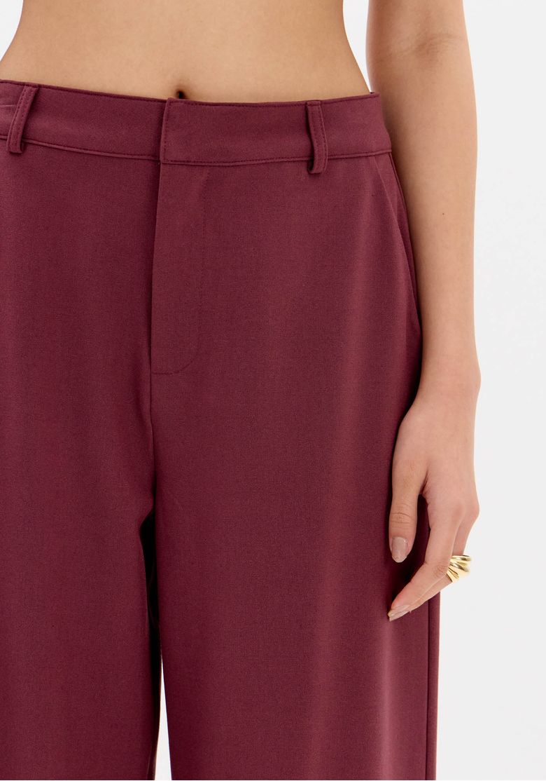 Modelo de costas usando conjunto com calça full length vermelha e top halter costas nuas, mostrando cós com passantes e caimento fluido