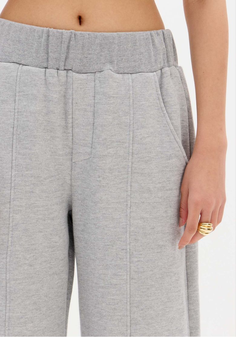 Detalhe do cós canelado elástico e bolso lateral da calça de moletom cinza com a mão da modelo ao lado