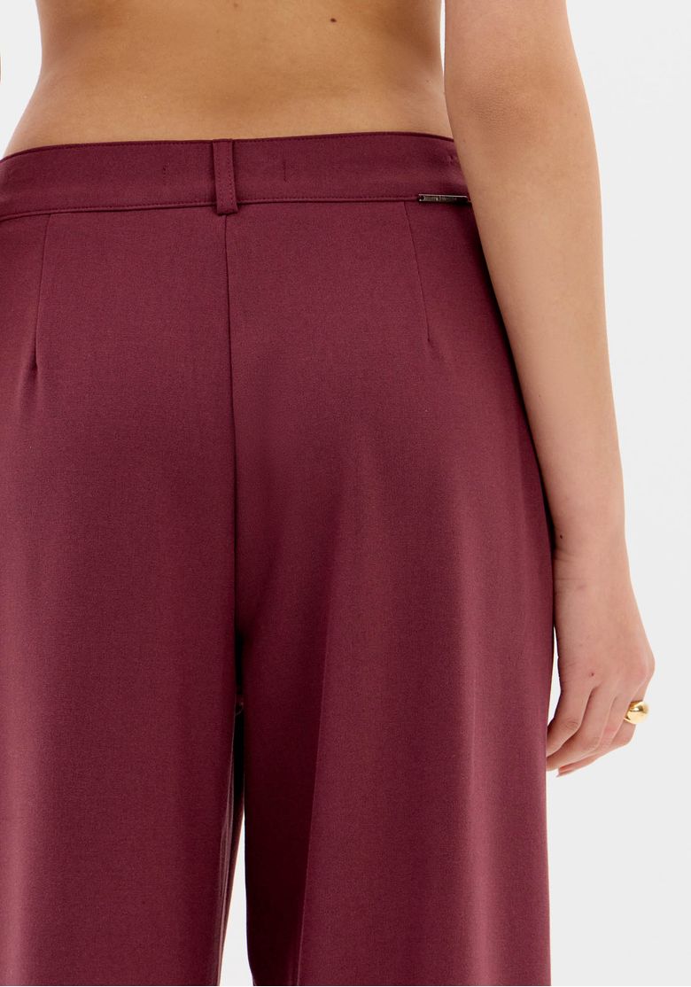 Detalhe traseiro do cós da calça full length vermelha, mostrando pence discreta e acabamento liso