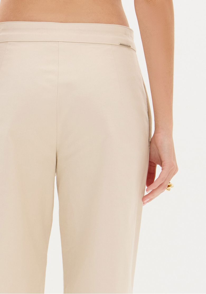 Detalhe do cós traseiro da calça bege, acabamento limpo sem bolsos traseiros aparentes e costura central