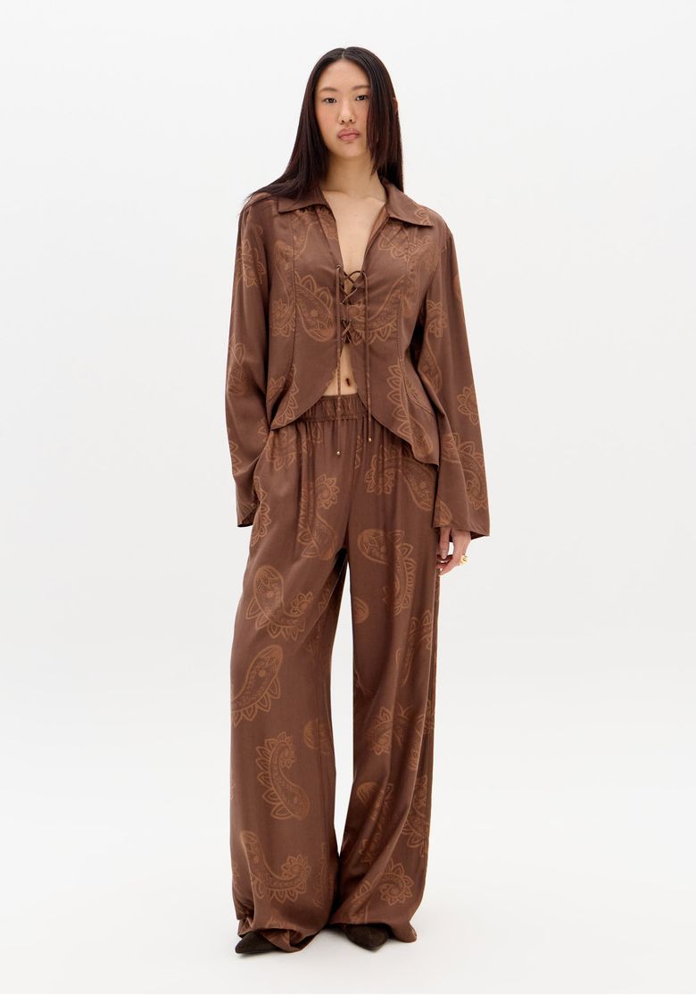 Modelo em look completo: calça pantalona marrom estampada paisley com blazer combinando e cós elástico à vista, visual boho chic