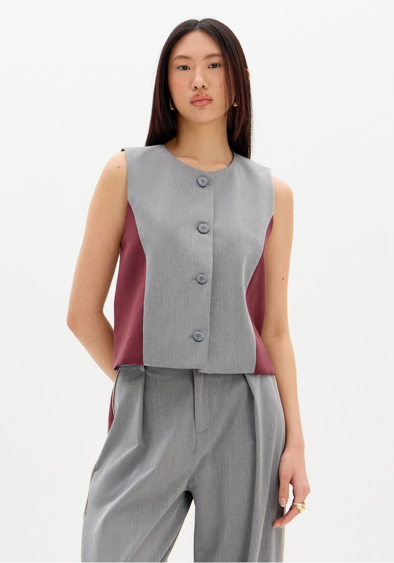 Modelo vestindo colete alfaiataria curto bicolor com painel frontal cinza e laterais vinho, vista 3/4 - colete curto feminino para trabalho