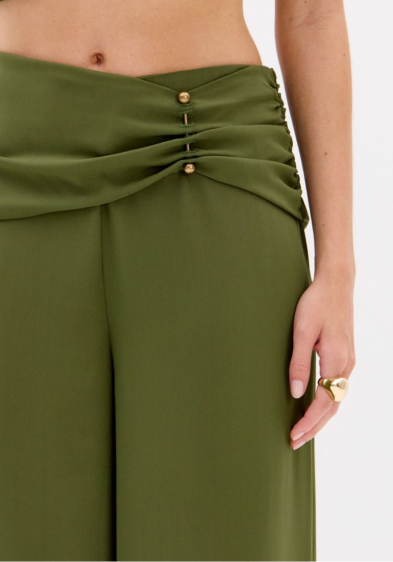 Detalhe traseiro do cós da calça pantalona verde com zíper invisível e botão dourado, mostrando o acabamento e as costuras de maneira detalhada.