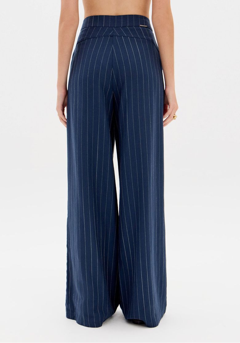 Modelo de costas usando conjunto risca-de-giz azul, mostrando o ajuste na cintura e o caimento fluido da calça