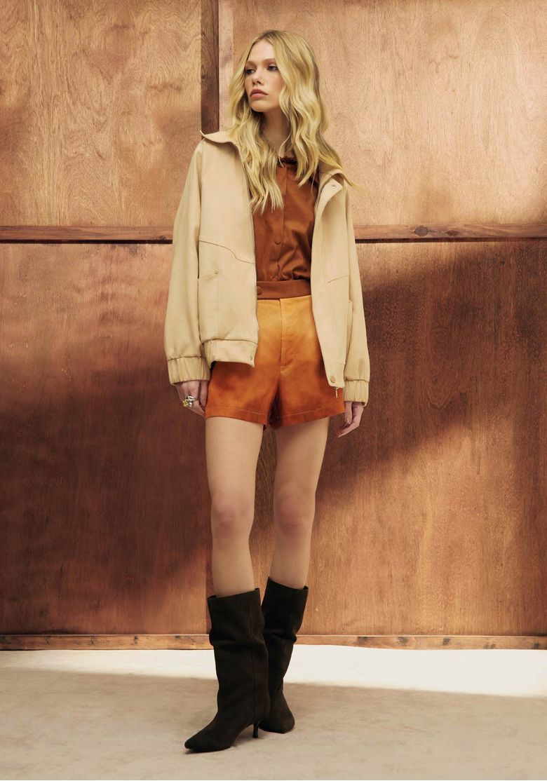 Mulher usando jaqueta bomber bege em camurça sintética, look utilitário com shorts marrom e botas pretas