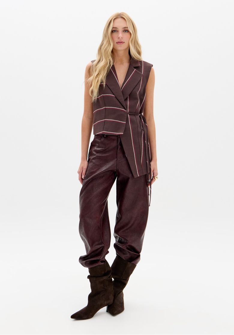 Imagem full body do colete assimétrico listrado com calça de couro vinho e botas camurça, look workwear urbano
