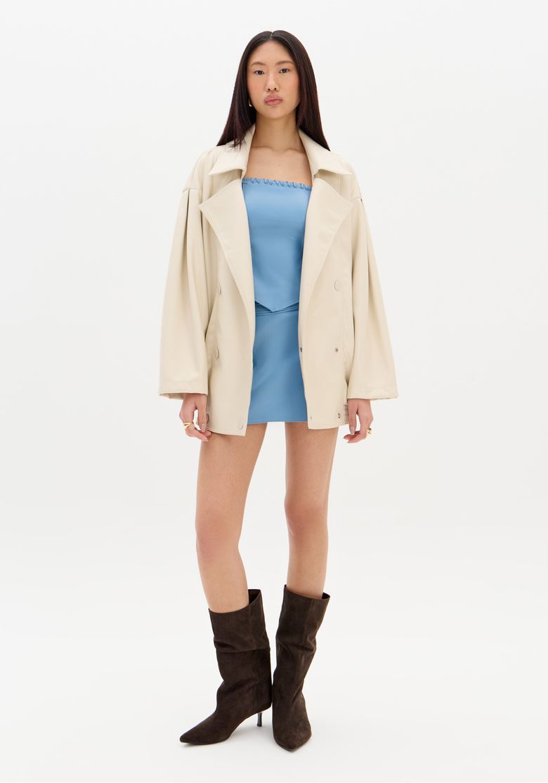 Modelo vestindo saia mini azul com casaco bege e botas marrons.