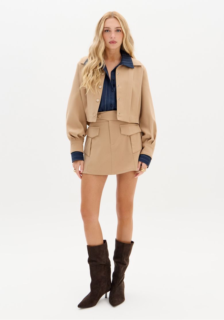 Modelo vestindo saia curta bege com camisa listrada e botas.