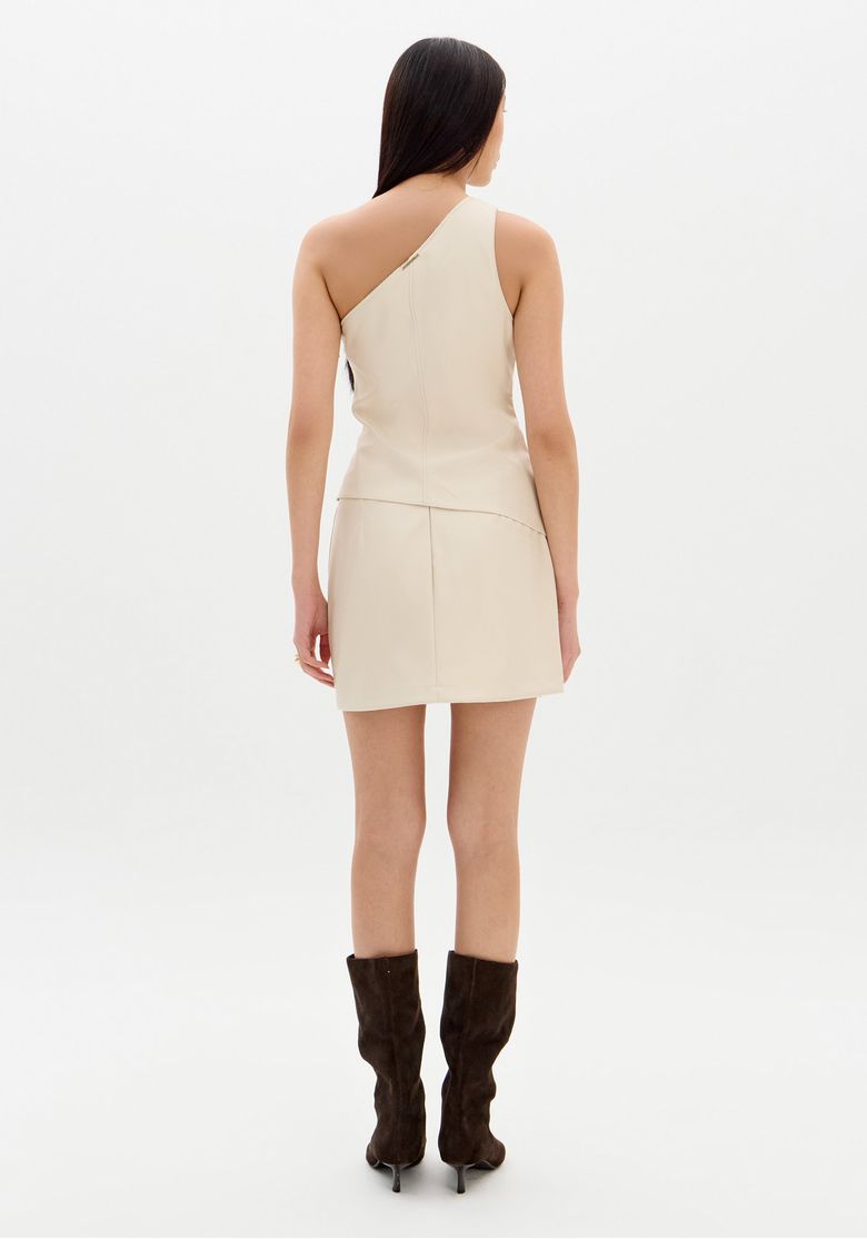 Vista traseira da modelo com saia mini PU bege exibindo costura central e comprimento curto, look completo com bota