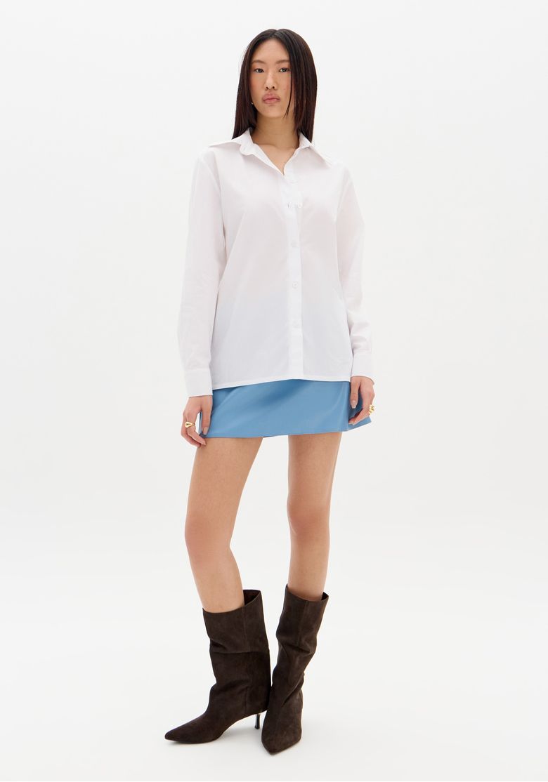 Modelo vestindo saia mini azul com camisa branca e botas marrons.
