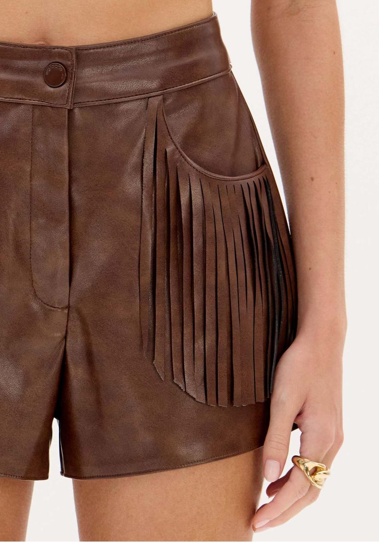 Visão frontal do short curto marrom em PU com cintura média e fechamento por botão, mostrando as franjas sobre os bolsos