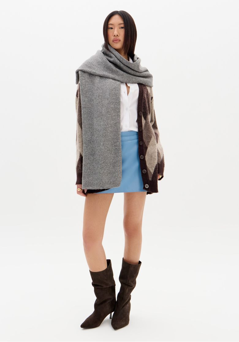 Modelo vestindo saia mini azul com cardigan xadrez e cachecol cinza.