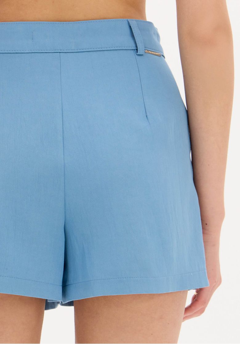 Vista-traseira-do-look-com-jaqueta-caramelo-sobre-short-saia-azul-evidenciando-comprimento-curto-e-caimento