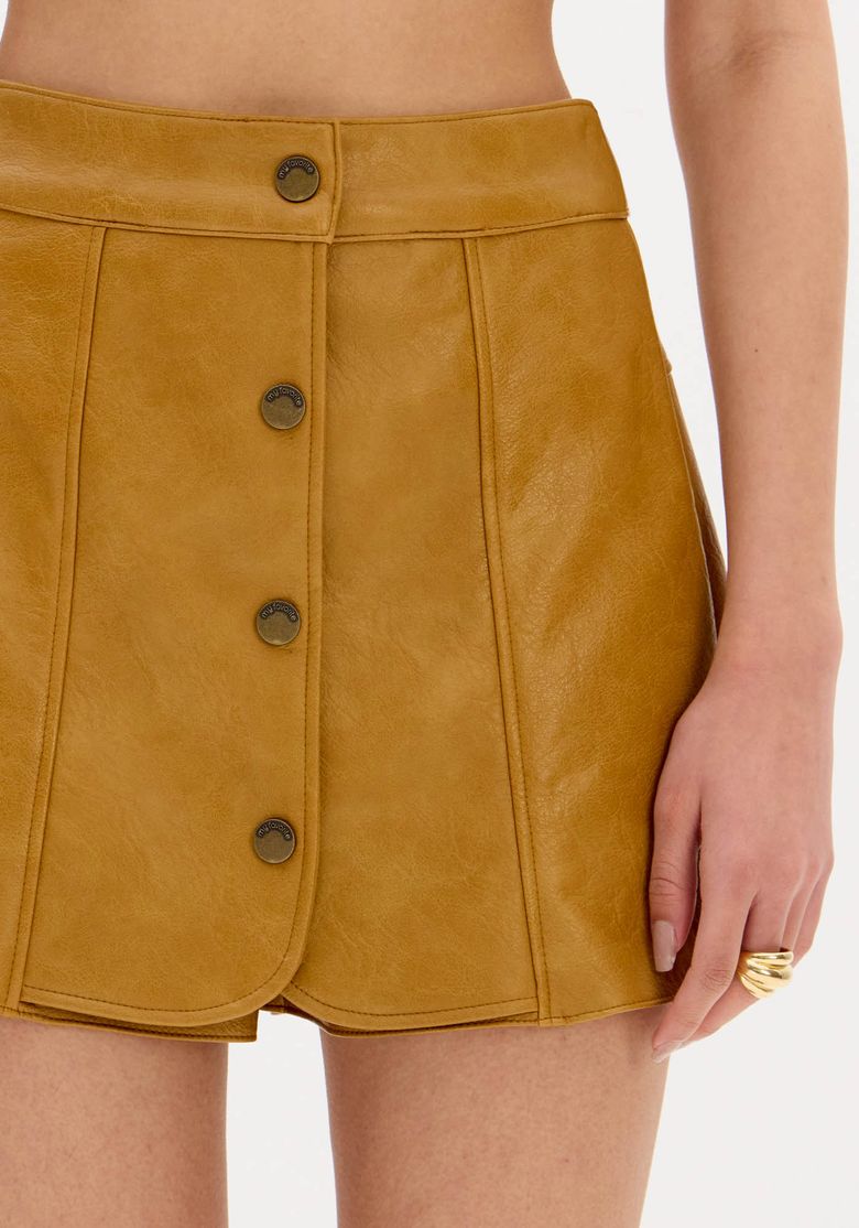 Close-do-cos-medio-do-short-saia-PU-bege-destacando-o-acabamento-da-costura-e-a-textura-acetinada-do-material-sintetico.