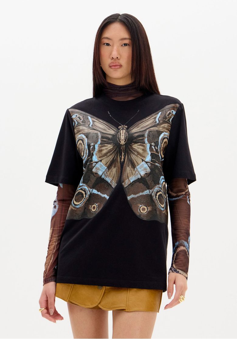 Modelo vestindo t-shirt oversized preta com estampa de borboleta, vista frontal.