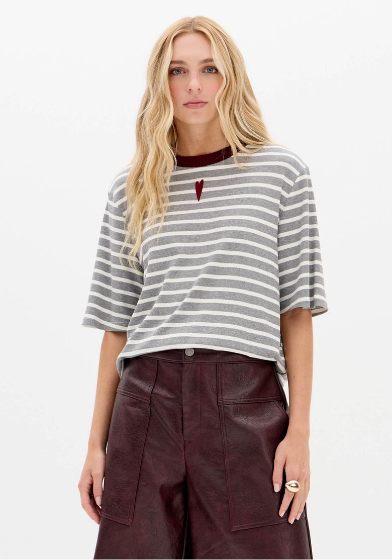Modelo usando camiseta listrada oversized cinza e branco vista frontal, gola canelada vinho e corte solto combinado com calça vinho