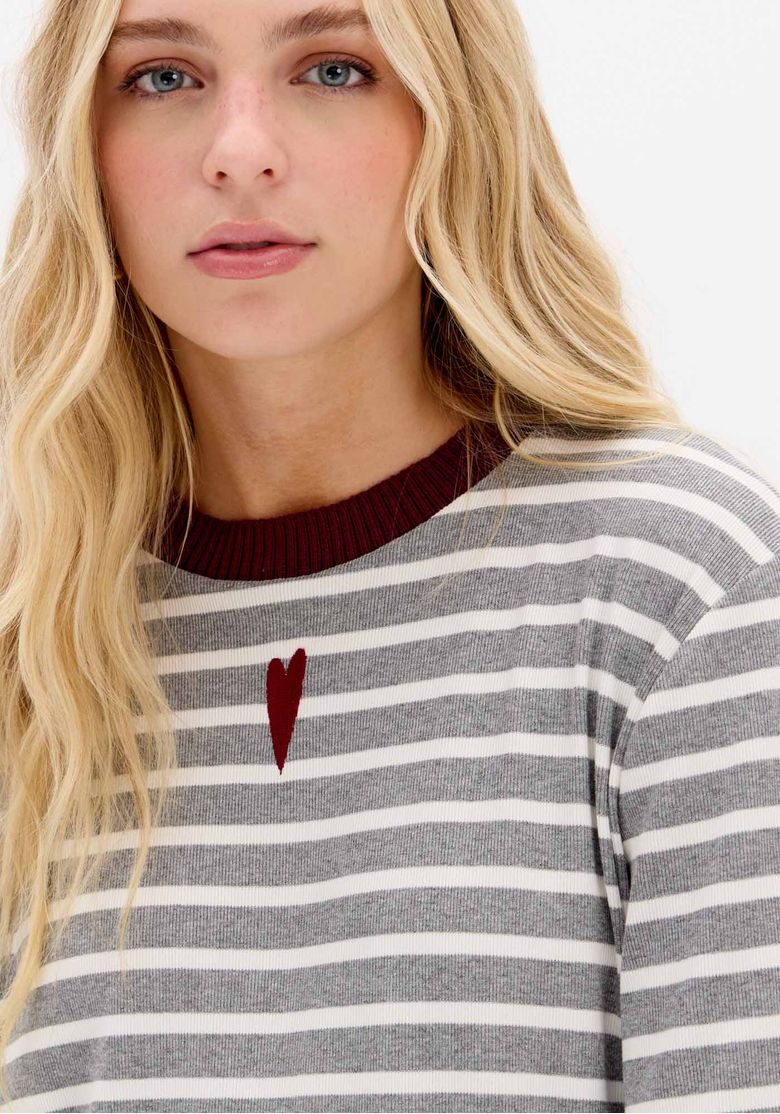 Camiseta listrada oversized vista frontal em corpo inteiro, mangas curtas largas e barra reta sobre calça vinho