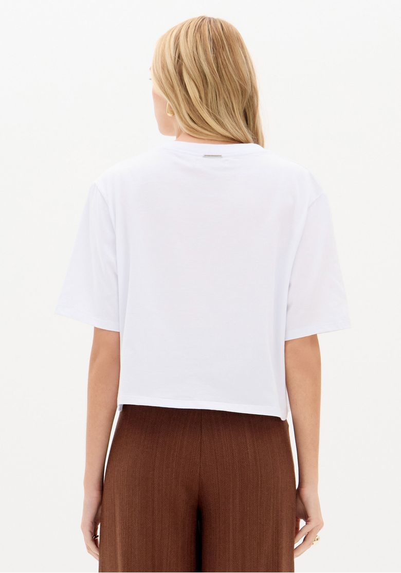 Vista traseira da camiseta oversized branca mostrando barra reta e caimento solto