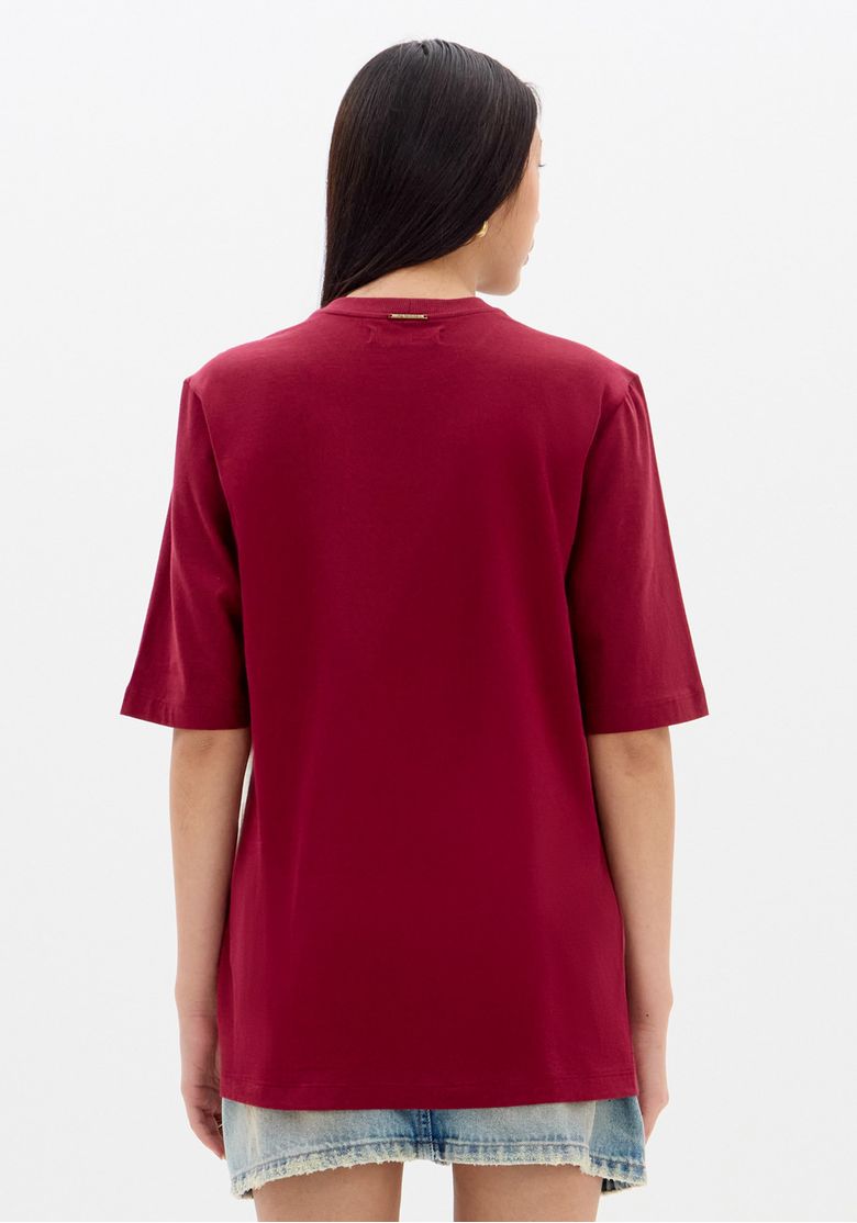 Vista traseira da camiseta oversized bicolor vermelha mostrando comprimento alongado, barra reta e caimento solto sobre saia jeans