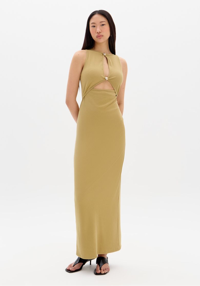 Modelo em pé utilizando vestido canelado super midi bege, visão frontal exibindo caimento ajustado e recortes com aviamentos metálicos.