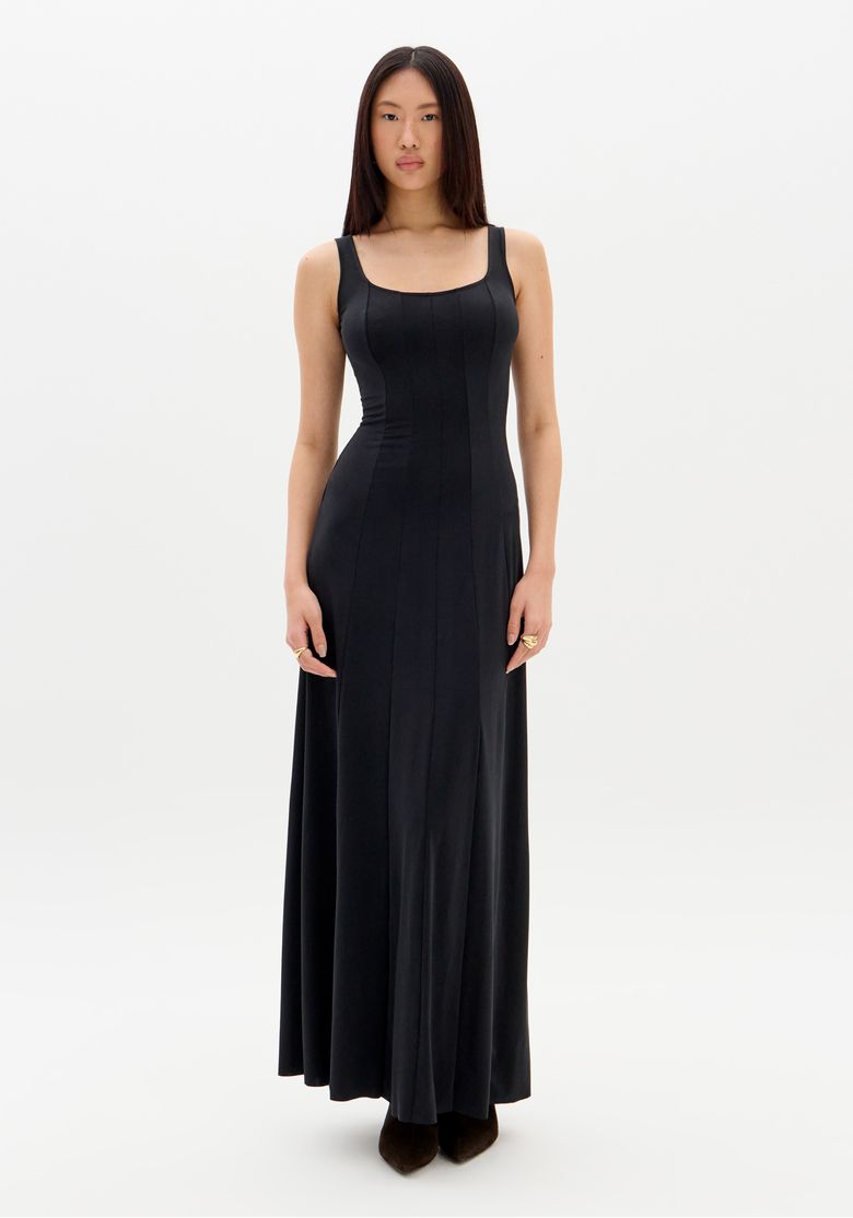 Modelo frontal usando vestido super midi preto com alças largas e nesgas verticais, visual minimalista para eventos noturnos