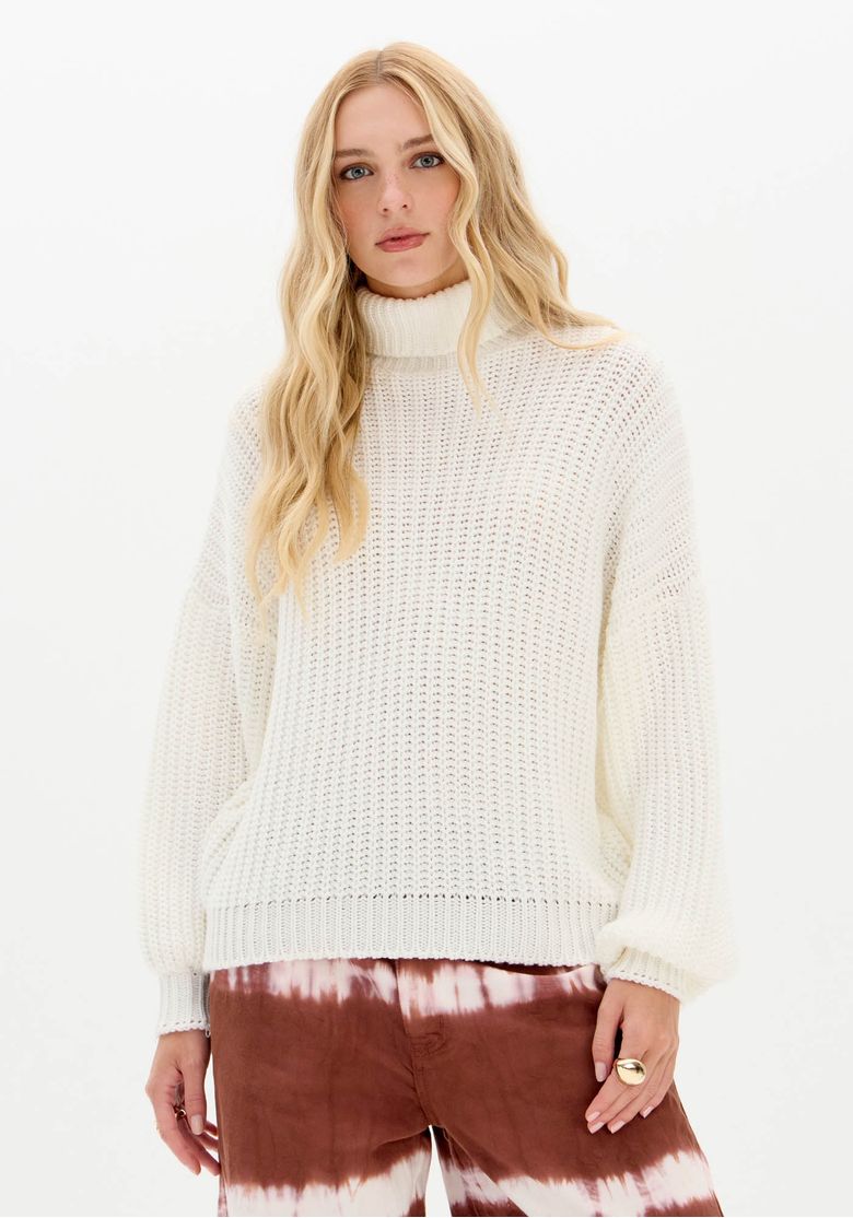Mulher vestindo blusa tricô branca gola alta oversized vista frontal mostrando ponto aberto e barra canelada