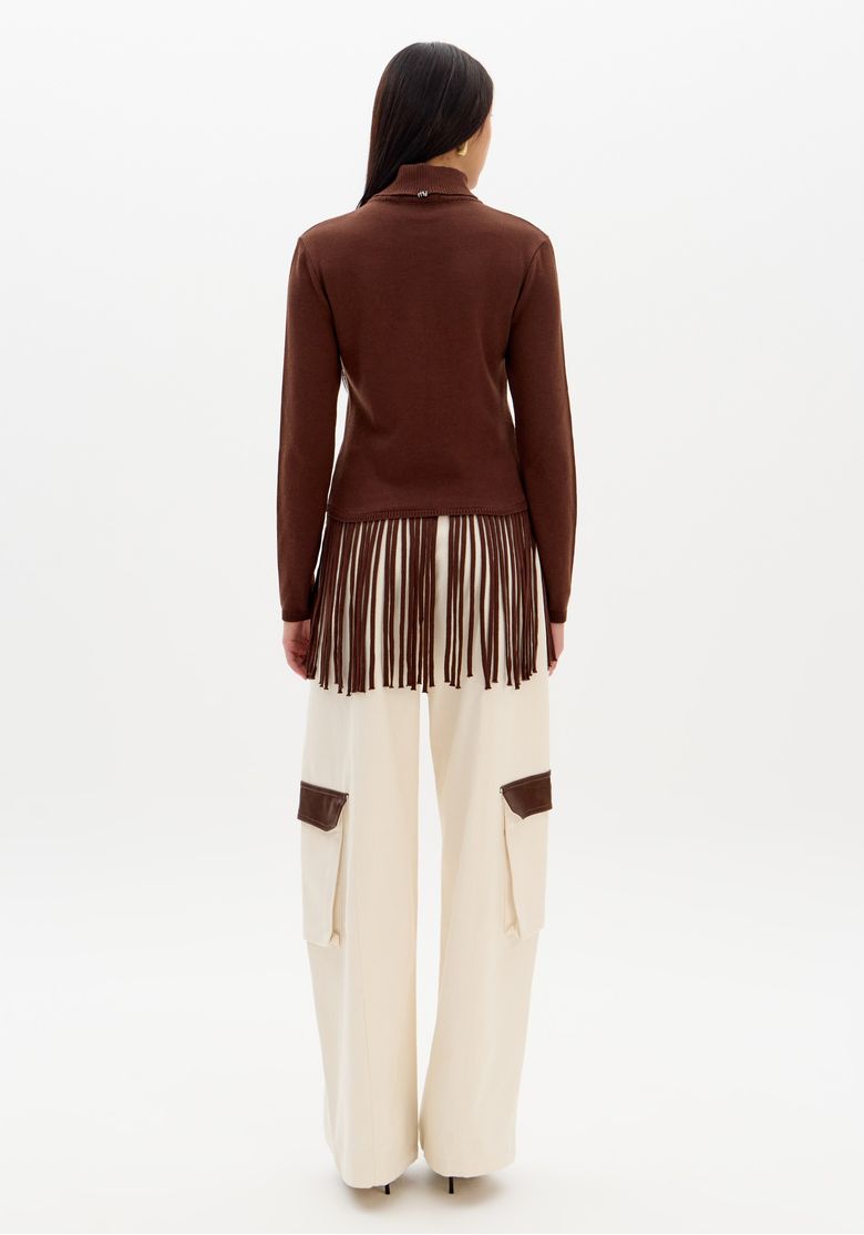 Modelo vestindo blusa de tricô marrom com gola alta e franjas, combinada com calça ampla off-white, criando um look urbano e casual