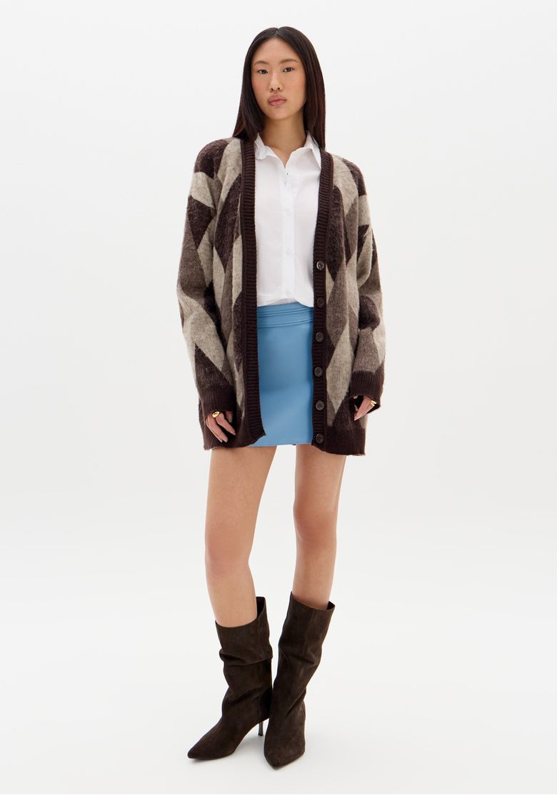 Modelo vestindo cardigã de tricô com saia azul e botas marrons.