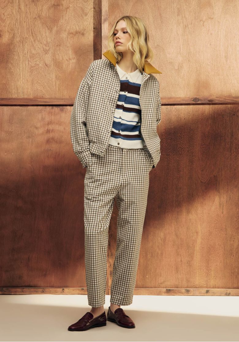 Modelo-usando-conjunto-xadrez--calca-carrot-cintura-alta-bege-com-blazer-oversize-e-mocassim-vinho-em-cenario-com-fundo-de-madeira---look-casual-urbano.