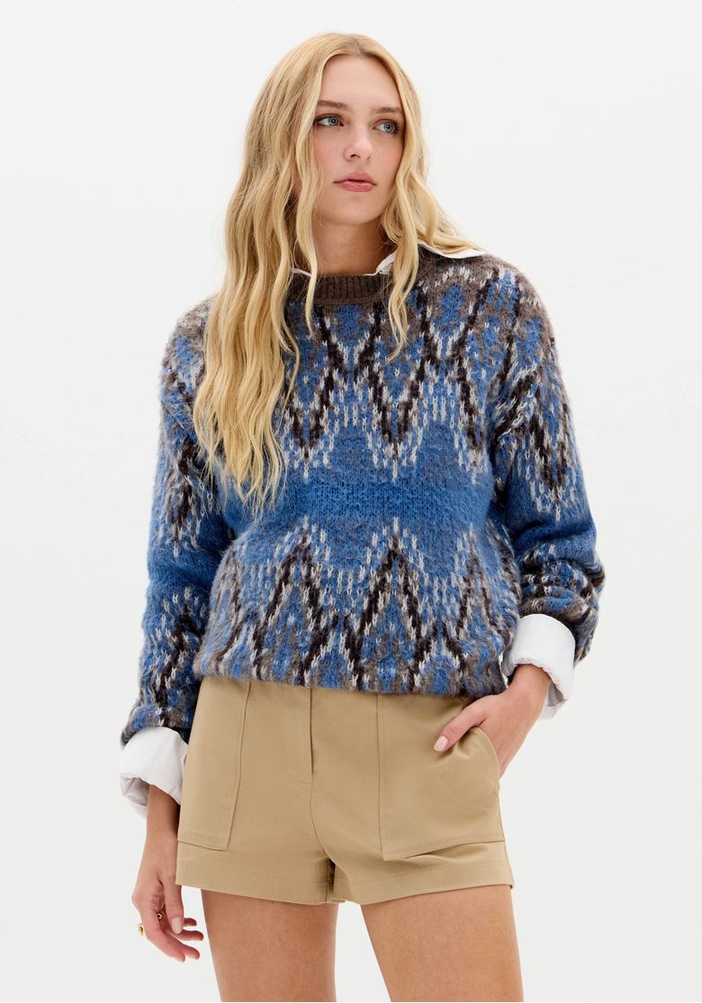Modelo com suéter de tricô azul oversized de mangas longas e shorts bege em visual casual