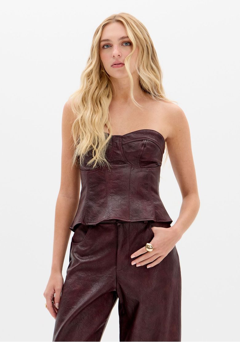 Vista das costas da blusa corset vinho em PU mostrando zíper metálico traseiro e recortes estruturados na barra